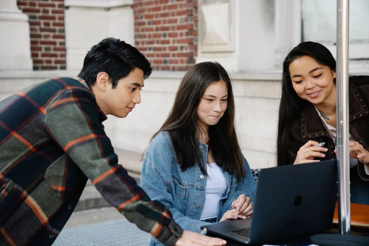 Three university students reviewing information together on a laptop on campus.