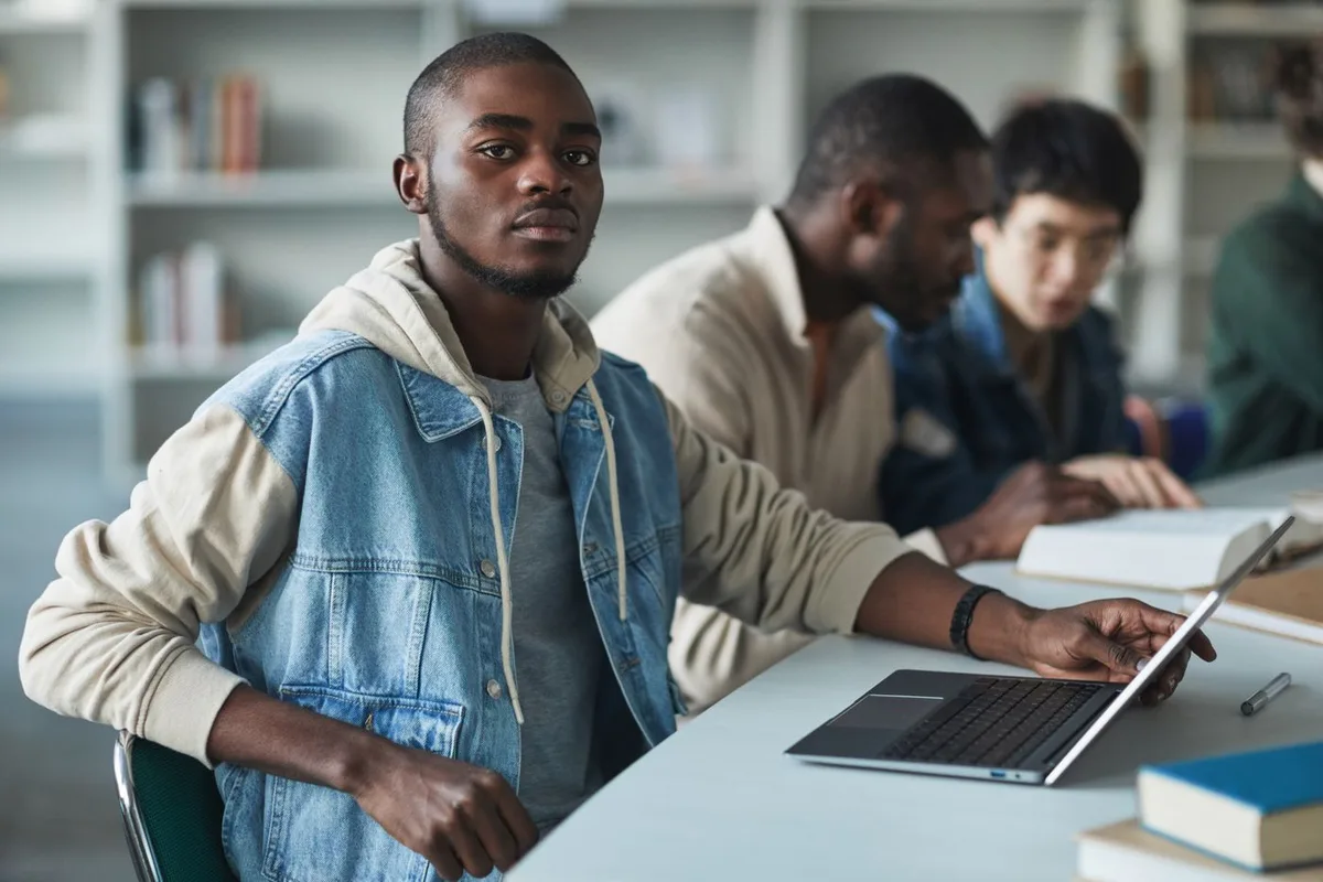 A university student using a laptop with fellow students studying nearby.