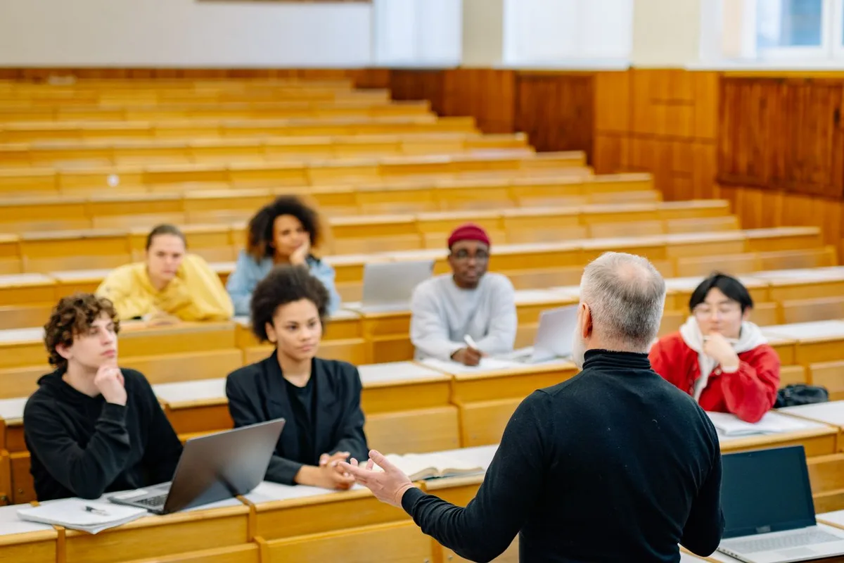 A lecturer leading an in-person university session with students using laptops.