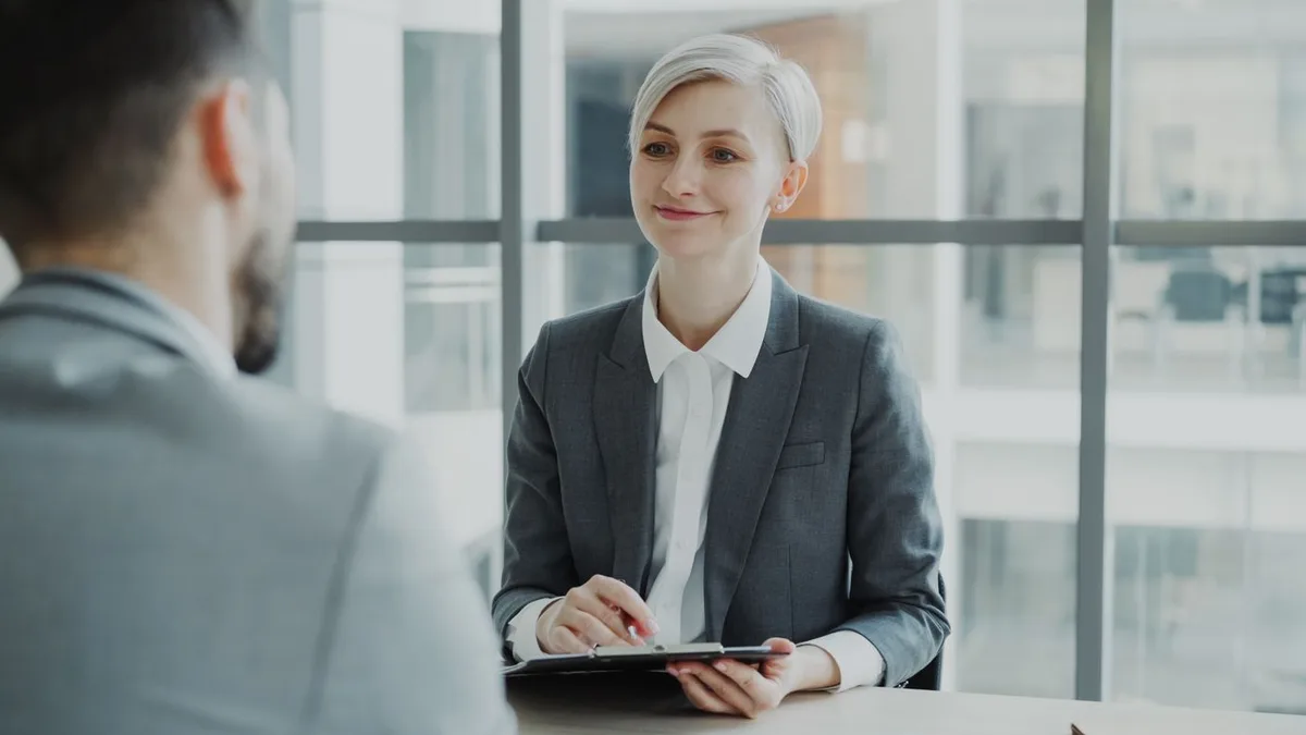 A hiring manager holding a clipboard while interviewing a candidate.